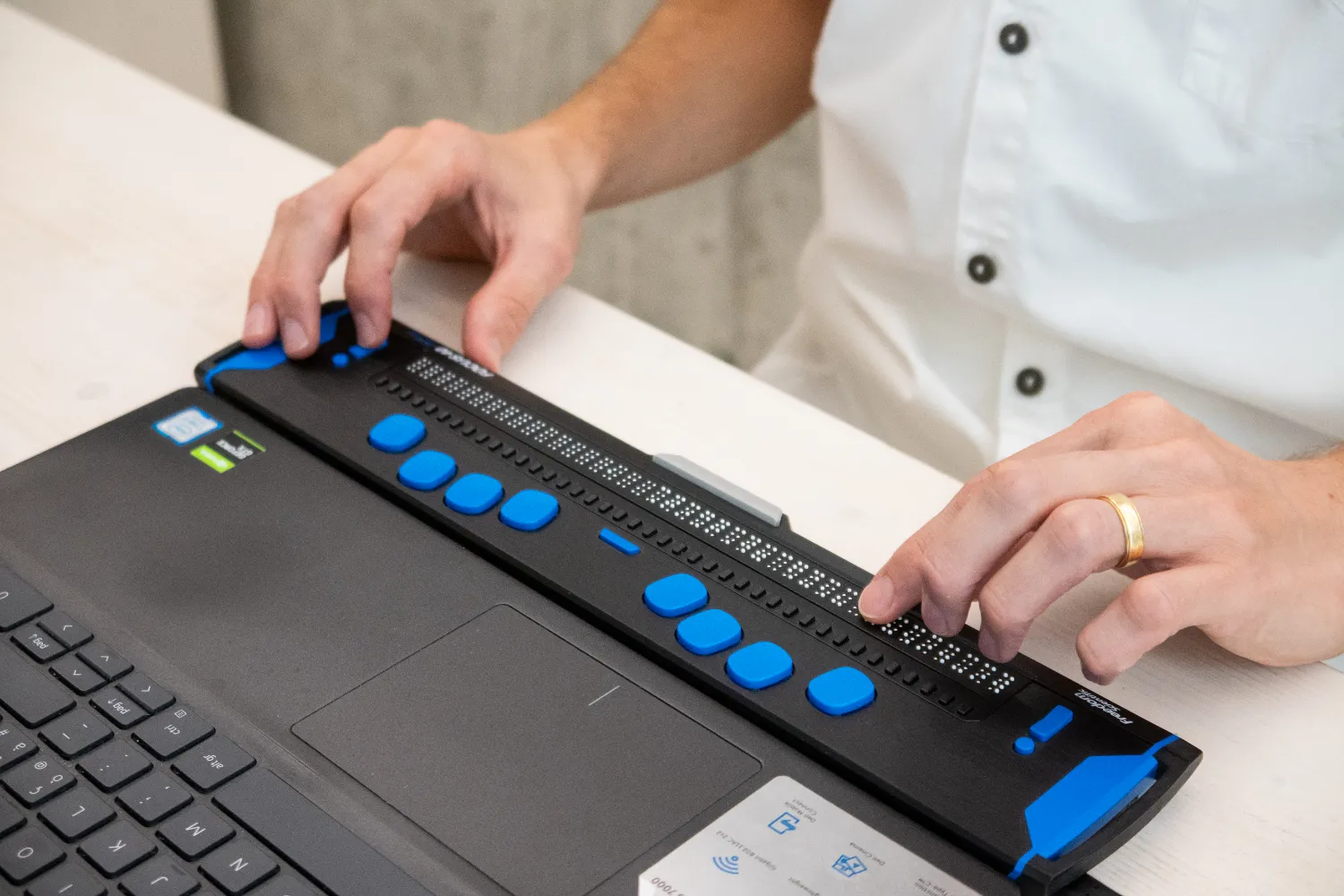 Dettaglio delle mani di una persona che utilizza lo schermo Braille con il suo computer